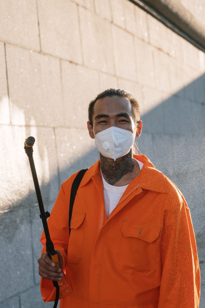 Man wearing protective coveralls and face mask spraying outdoors.