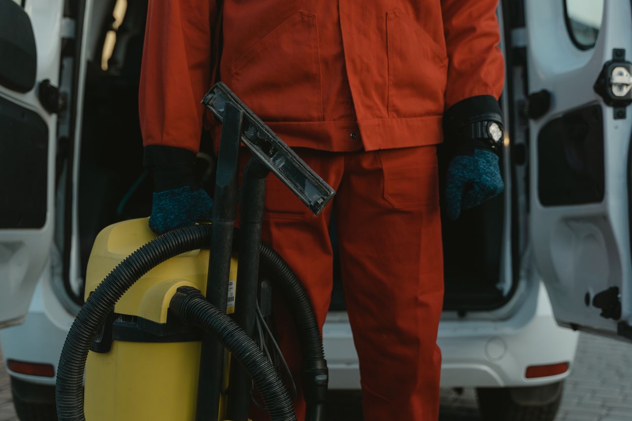 creative-approach-img A professional cleaner in a red uniform holding a vacuum near a van, ready for service.